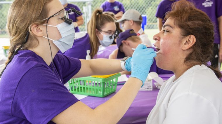 Volunteer cleans athletes teeth during a health screening