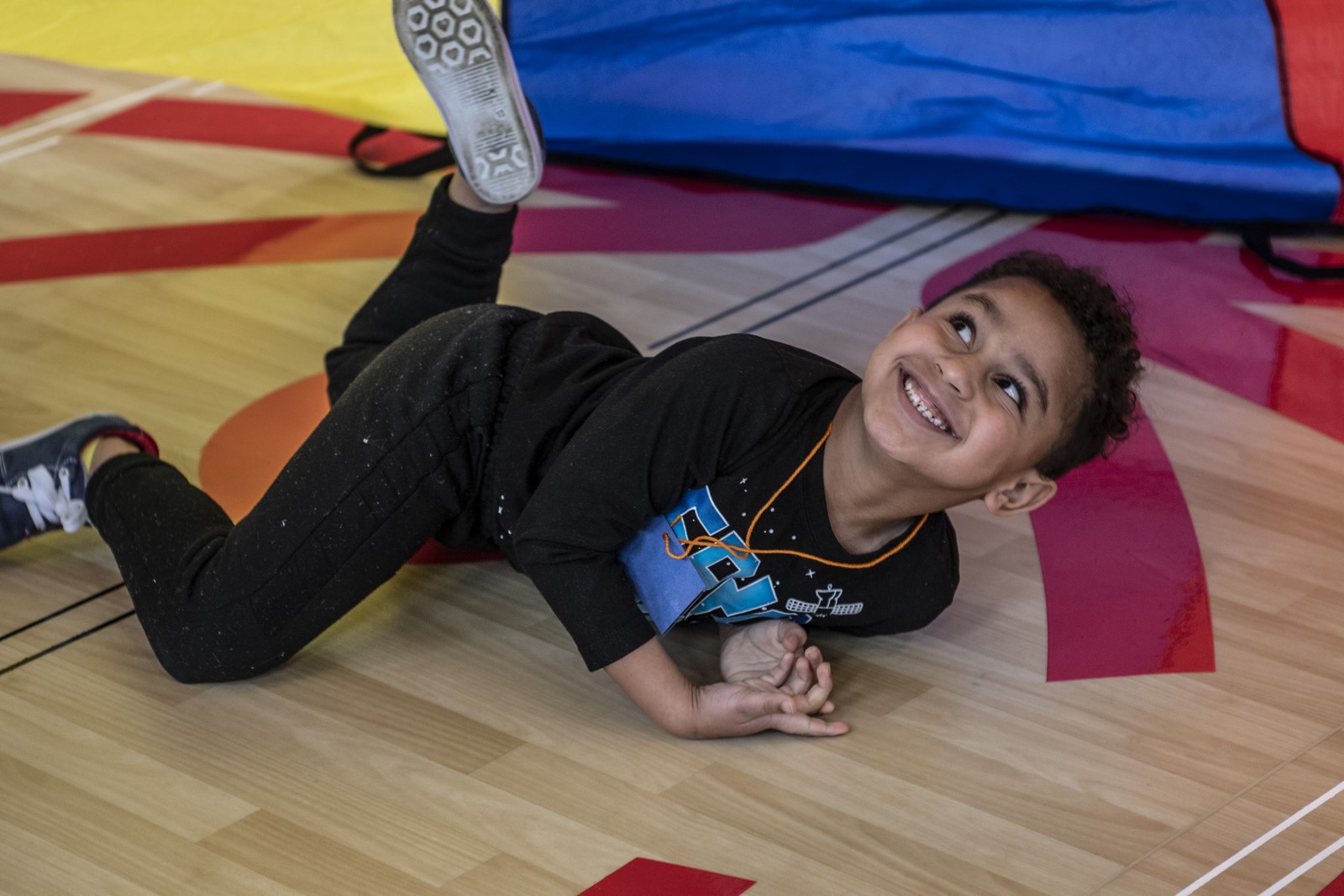 Young athlete laying on belly under a parachute and looking up while smiling