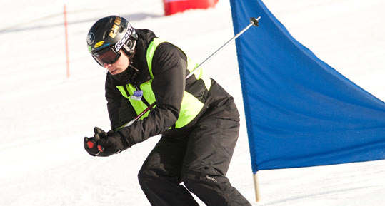 An athlete dressed in black skis down a hill past a blue marker