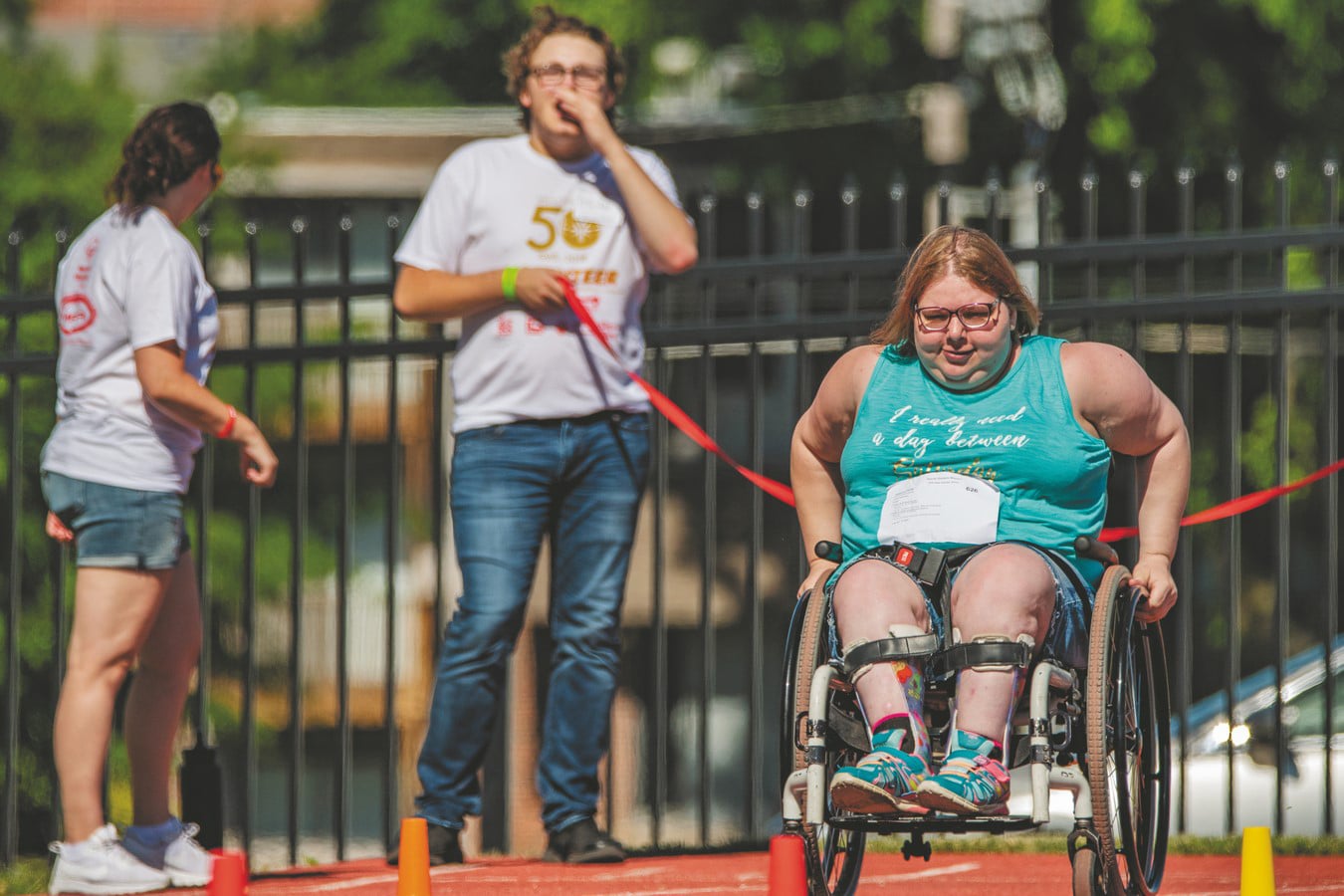 An athlete who uses a wheelchair races down the track while a volunteer looks on from behind