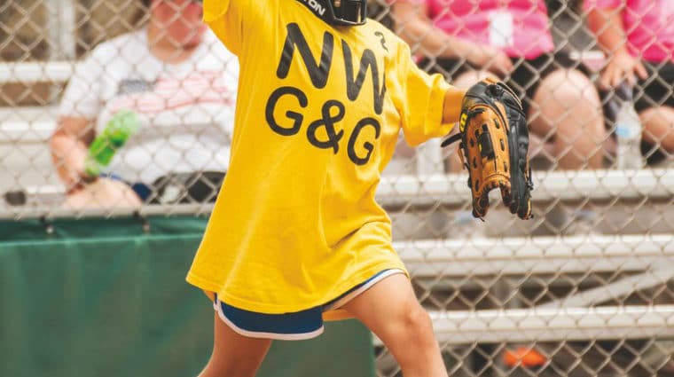 A young athlete playing catcher throws the softball back while wearing a black catcher's mask