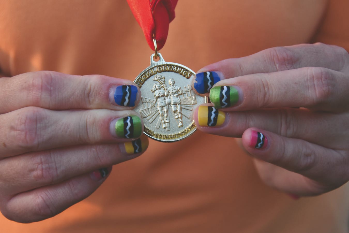 gold medal held in hands with colorful painted fingernails