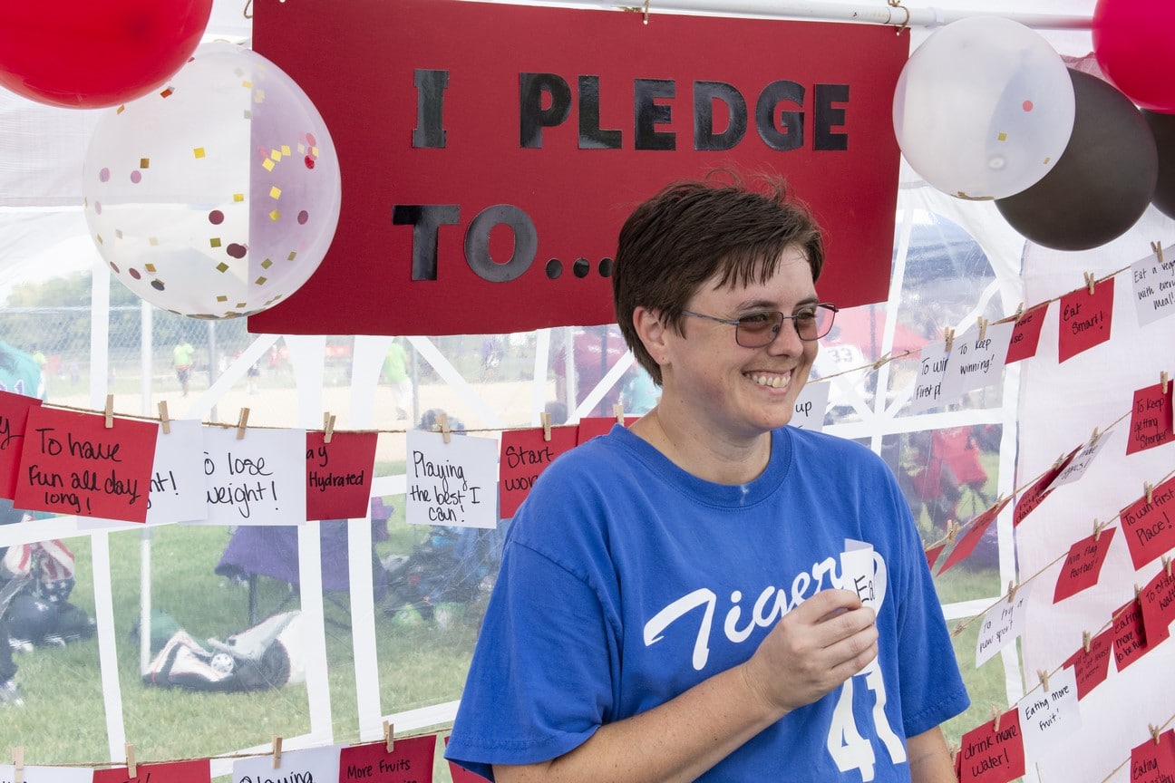 An athlete poses for a photo in front of a sign labeled "I pledge to..."