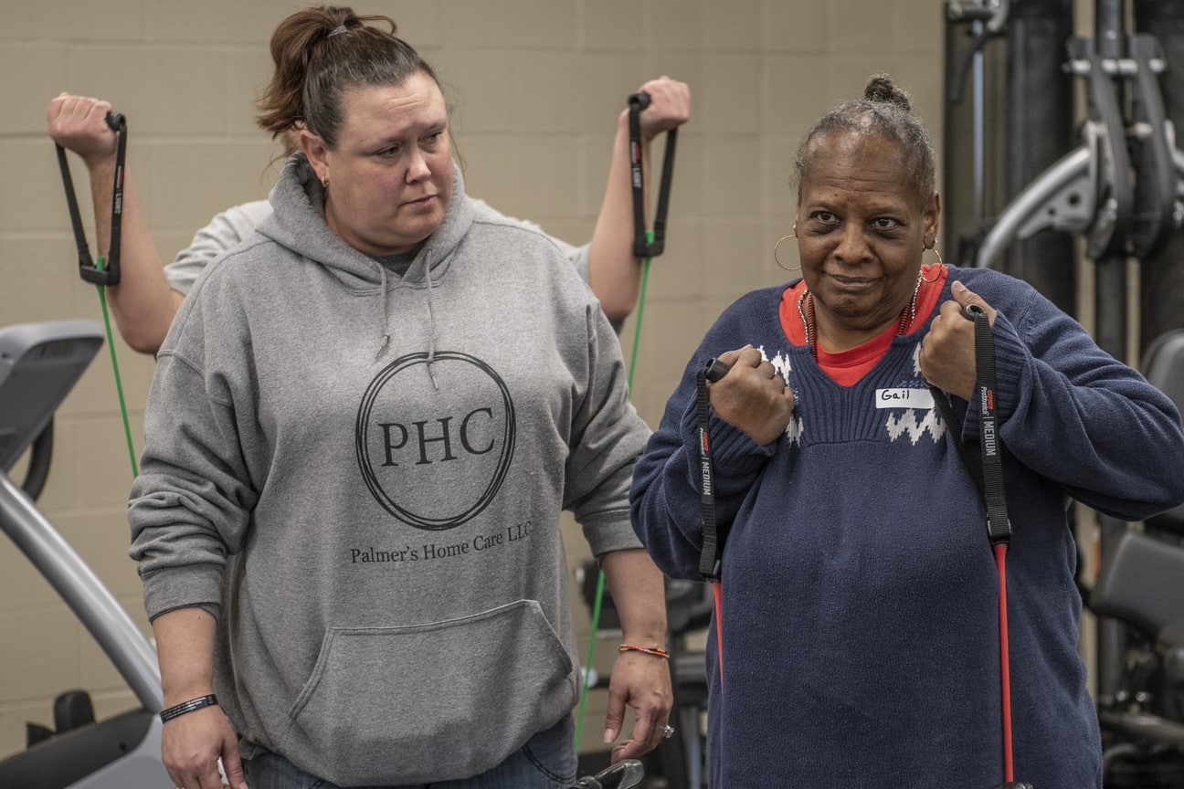 An athlete uses workout bands while a volunteer looks on