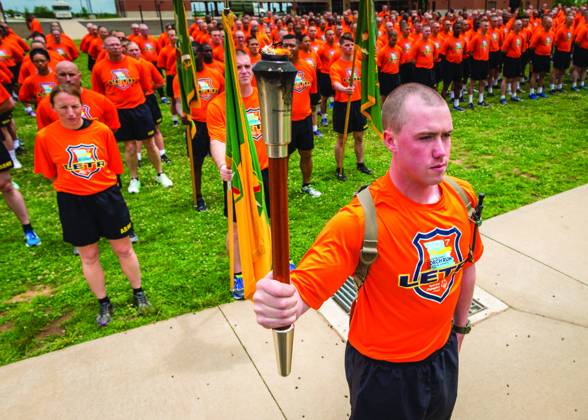 A person in an orange LETR shirt holds a lit torch with more than a hundred standing at attention behind them