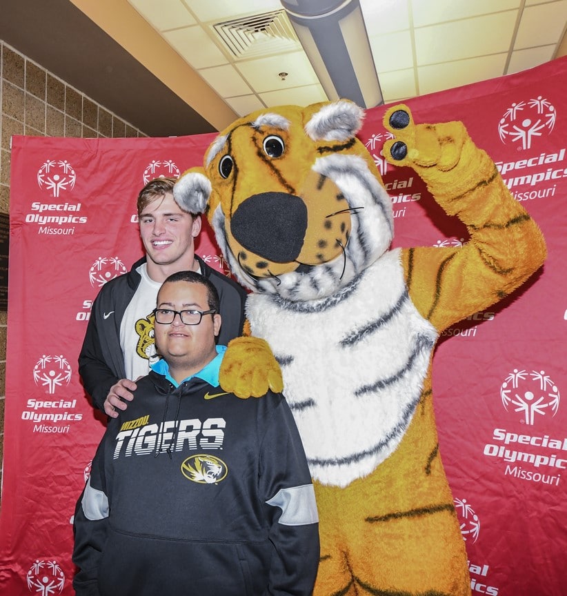 An athlete, a volunteer, and someone in a Truman the Tiger costume pose for a photo