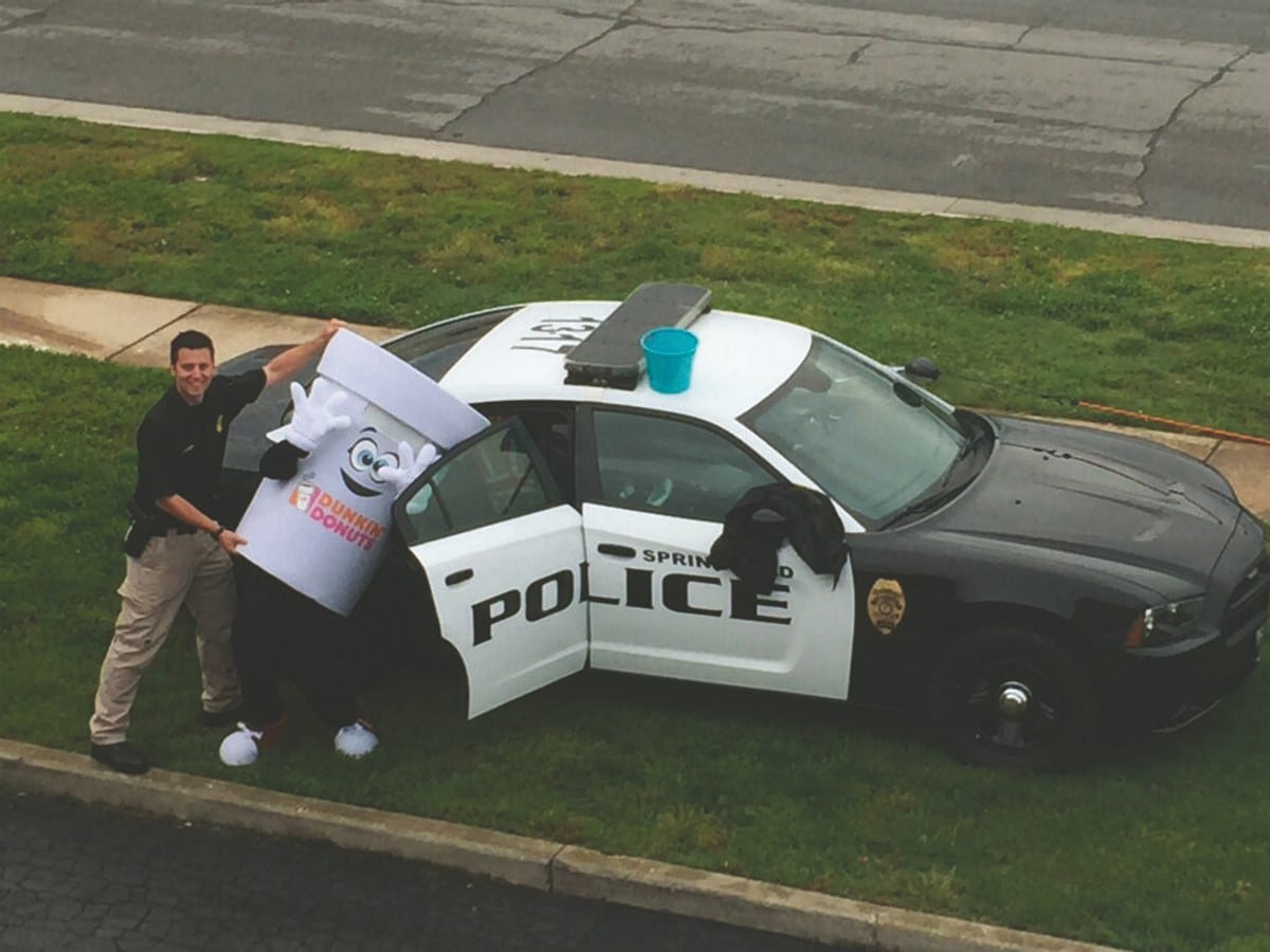 Police Officer pretending to put Dunkin Donuts mascot in the back of a cop car