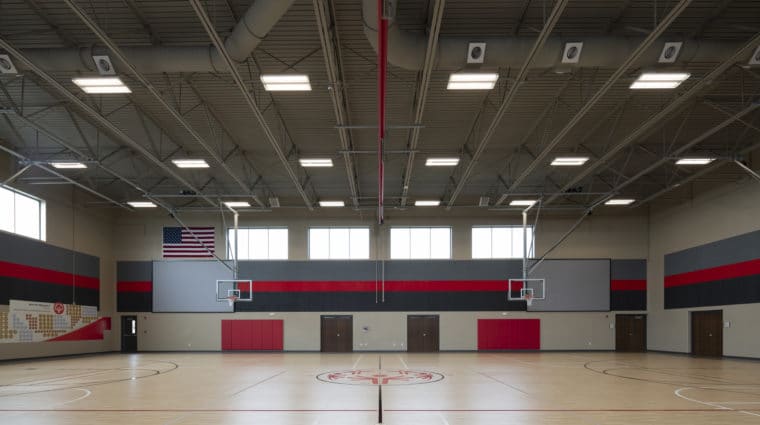 A gymnasium with two basketball hoops, two large screens, and a SOMO logo at center court