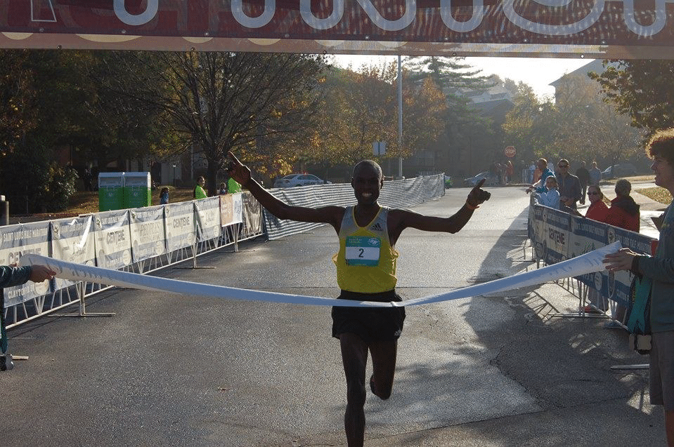 A runner crosses a finish line breaking the finish tape in the process