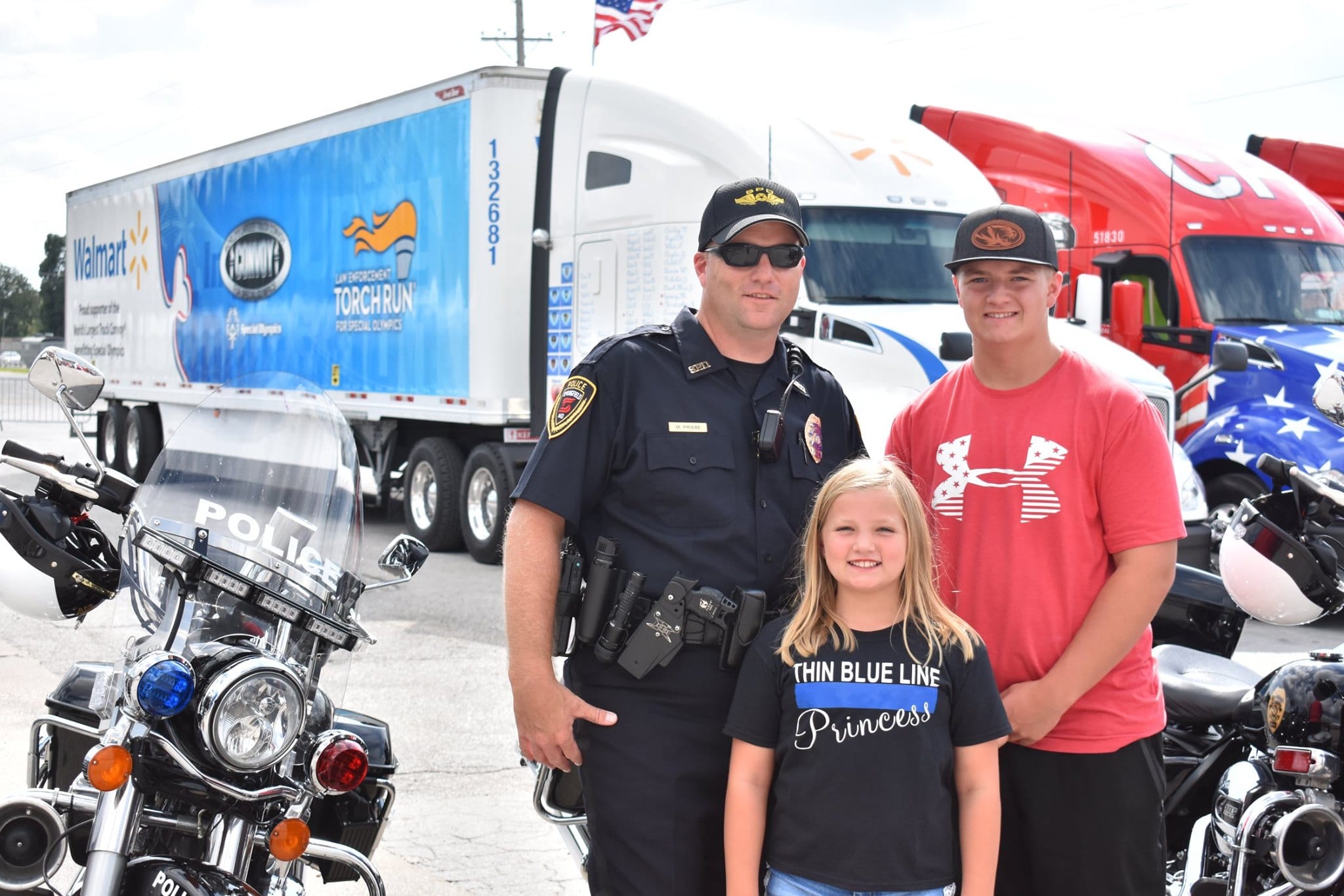 Sargent Mark Priebe poses for a photo with his two children in front of motorcycles and semi-trucks