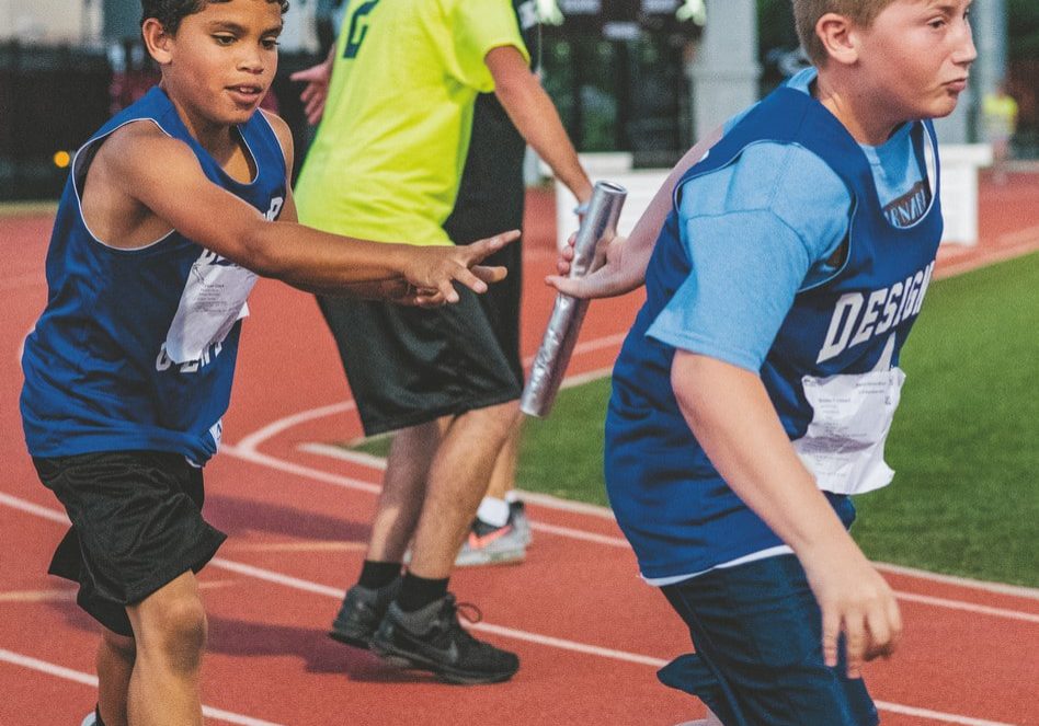 Two athletes perform a baton handoff during a track and field race