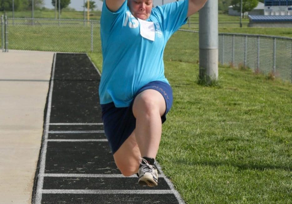 A long jump athlete flies through the air with arms outstretched as they are about to land in the sand