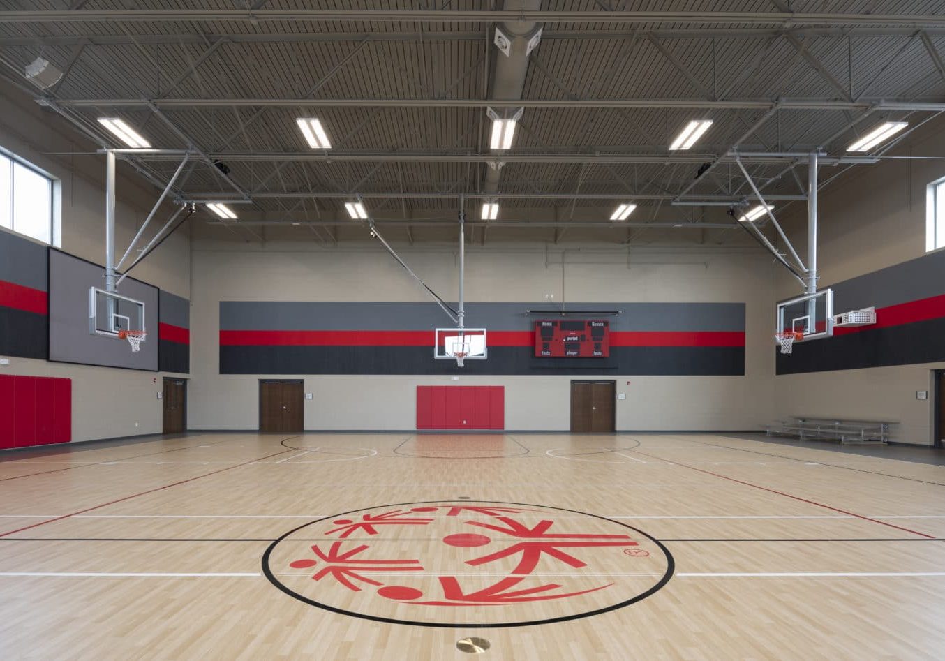 A gymnasium with three basketball hoops, a scoreboard, and a SOMO logo at center court